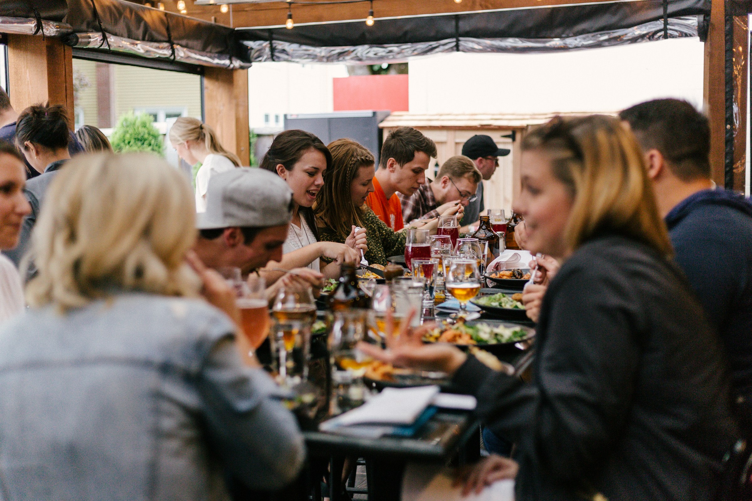 Vrienden praten en lachen aan een lange tafel met glazen bier en eten.